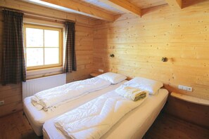 Une chambre dans un chalet en bois, avec deux lits, une fenêtre avec des rideaux et un plafond en bois.