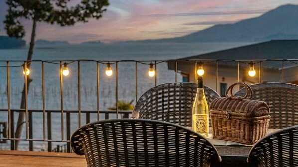 Un espace extérieur aménagé avec des chaises et une table en osier, une bouteille de vin et un panier en osier.