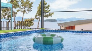 Ein Schwimmbecken mit Blick auf das Meer und die Berge, umgeben von Bäumen und einem Gebäude.