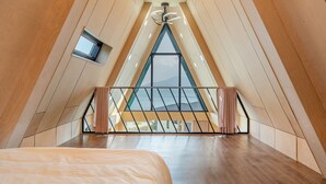 A modern attic bedroom with a sloped ceiling, a bed, a small window, and a view of the outdoors. - Sacheon Ara Private Pool Villa (Sacheon)