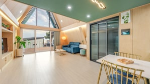A spacious living area with a large sliding glass door leading to a balcony, a blue sofa, a dining table with chairs, and a modern light fixture. - Sacheon Ara Private Pool Villa (Sacheon)