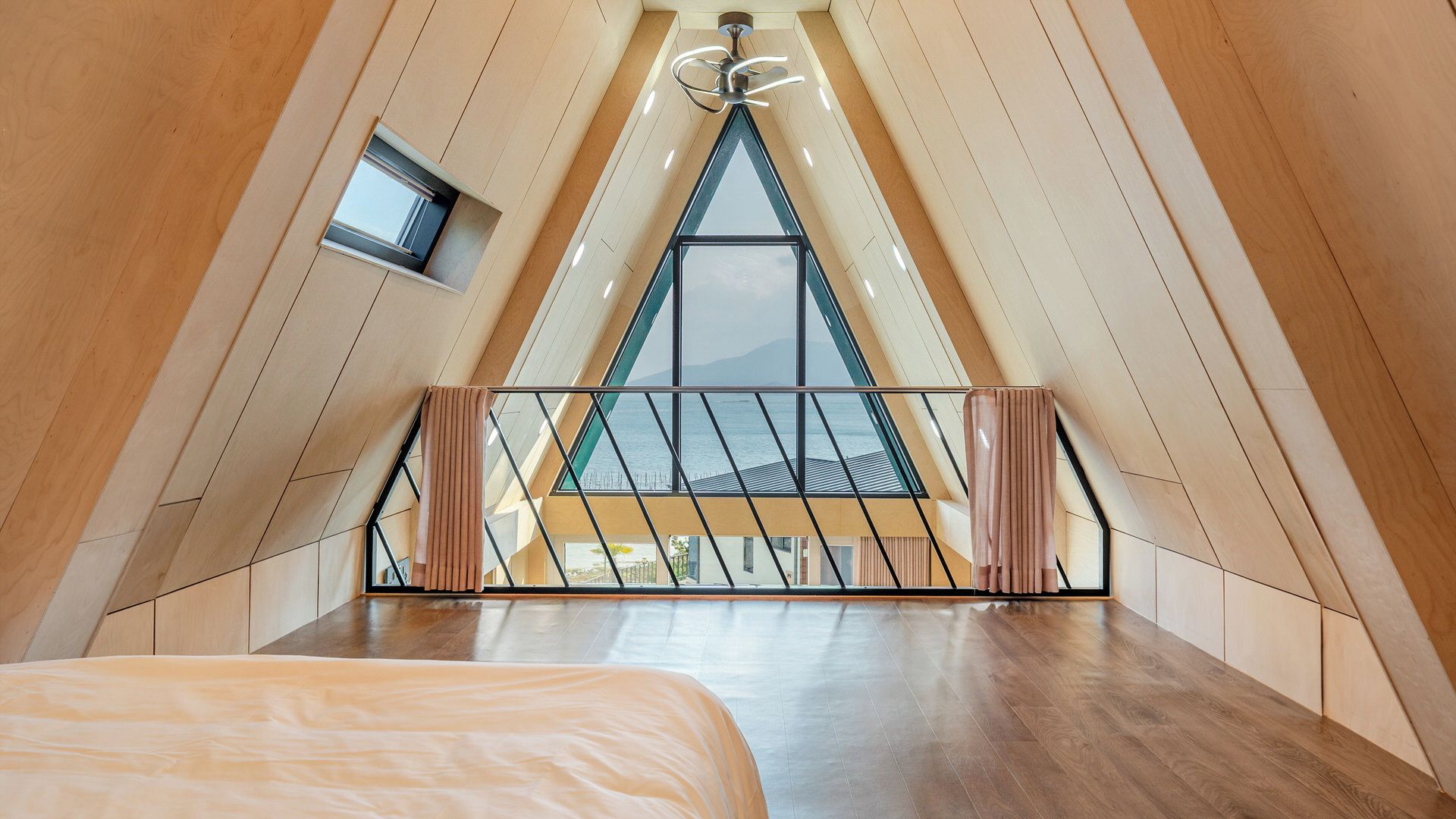 A high-ceilinged room with a sloped ceiling, a bed, a small window, and a view of the outdoors.