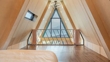A high-ceilinged room with a sloped ceiling, a bed, a small window, and a view of the outdoors.