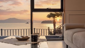 A room with a view of a sunset over water, a balcony with a railing, and a sofa. - Sacheon Ara Private Pool Villa (Sacheon)