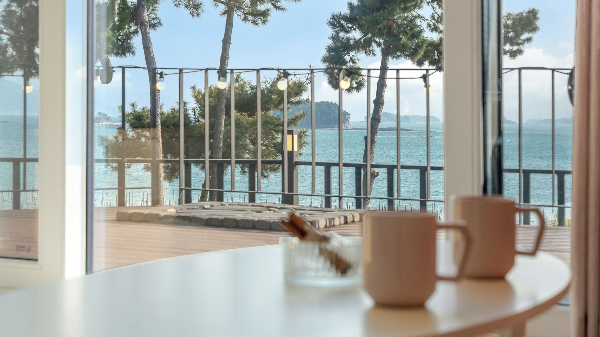 Un balcón con vista al mar, una barandilla y dos tazas sobre una mesa.
