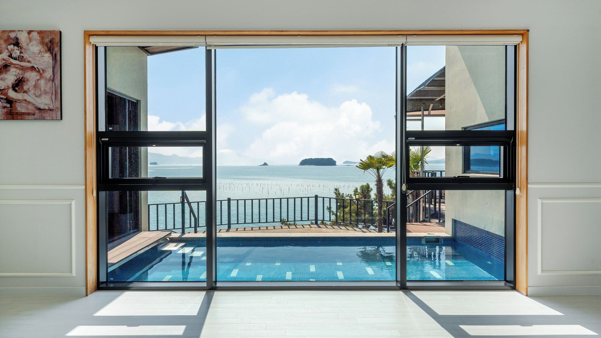 A modern room with a large sliding glass door leading to a pool area with a view of the sea and distant islands.