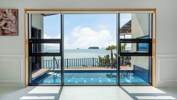A modern room with a large sliding glass door leading to a pool area with a view of the sea and distant islands.