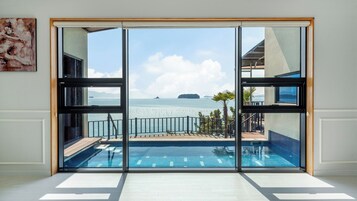 Una habitación moderna con un amplio ventanal corredera que da a una zona de piscina con vistas al mar y a islas distantes.