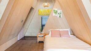 A bedroom with a sloped ceiling, a bed with white and pink bedding, a nightstand with a lamp, and a wall-mounted artwork. - Sacheon Ara Private Pool Villa (Sacheon)