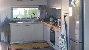A modern kitchen with white cabinets, a stainless steel refrigerator, and a window with curtains. - La Casa del Sol Sea View Sunset Jacuzzi (Aegina)