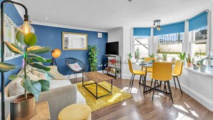A modern living room with a dining area, featuring a sofa, a coffee table, and a dining table with yellow chairs. - Seaside Gem Apartment By My Getaways (Brighton)
