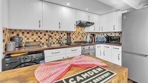 A modern kitchen with white cabinets, a wooden countertop, and a built-in washing machine. - Seaside Gem Apartment By My Getaways (Brighton)