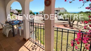 A balcony with a table set for dining, a view of the sea, and a garden with pink flowers. - Apartment in residence closed, with big barbecue comun, 2 swimming pool.  2 bedrooms , parking. (Peníscola/Peñíscola)