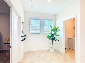 A hallway with a potted plant, a door, a window, and a laundry area.
