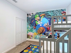 A room with a mural of Mario and Luigi, a white door, a bunk bed, and a colorful rug.