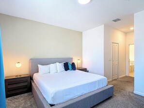Habitación de hotel con una cama grande, dos mesitas de noche, una mesilla y un baño visible a través de una puerta abierta.