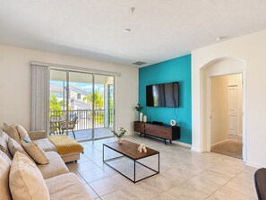 A modern living room with a sofa, coffee table, and a flat-screen TV mounted on a teal wall.