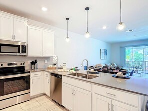 Una cocina moderna con armarios blancos, electrodomésticos de acero inoxidable e iluminación colgante.