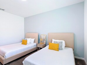 Habitación de hotel con dos camas individuales, cada una con cabecera, mesita de noche y lámpara.