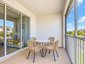 Un balcón con una mesa redonda y cuatro sillas, un ventanal corredero y vistas a una zona residencial.