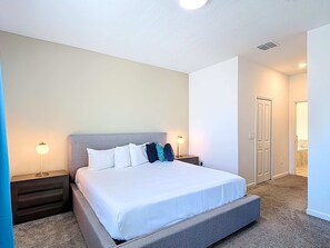 A hotel room with a large bed, two bedside tables, a nightstand, a door, and a bathroom visible through an open door.