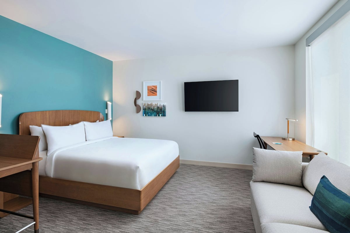 A modern hotel room with a large bed, a sofa, a desk, and a flat-screen TV.