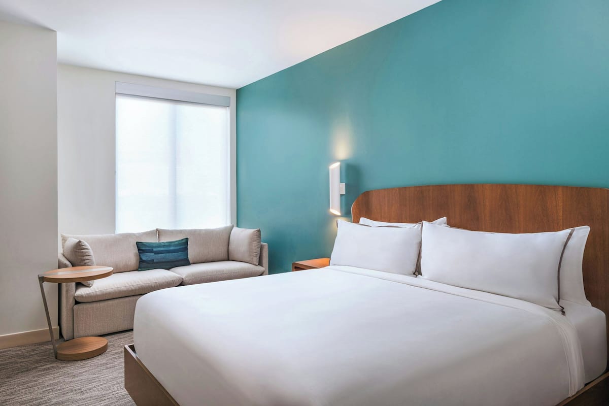 A hotel room with a large bed, a sofa, a small table, and a nightstand.