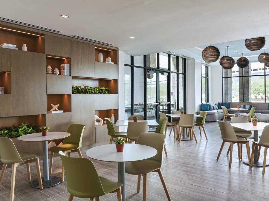 Ein modernes Interieur mit runden Tischen und grünen Stühlen, Holzregalen mit Dekoration und großen Fenstern mit Blick.