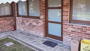 A brick building with large windows, a fire extinguisher, and a yellow delivery bag on the porch. - At the home of "Nuccia" (Foglizzo)