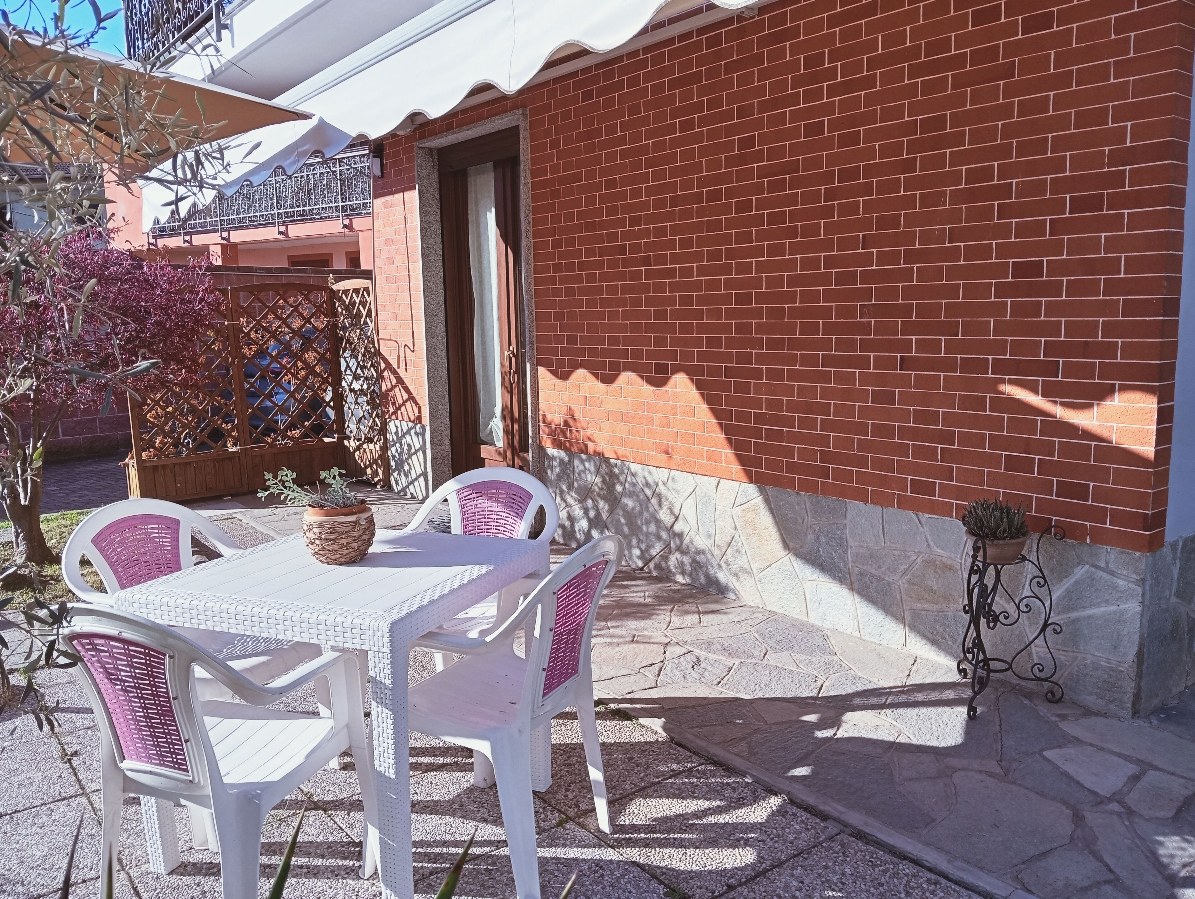 Eine Terrasse im Freien mit einem weißen Tisch und Stühlen, einer Backsteinmauer und einem Topfpflanzen.
