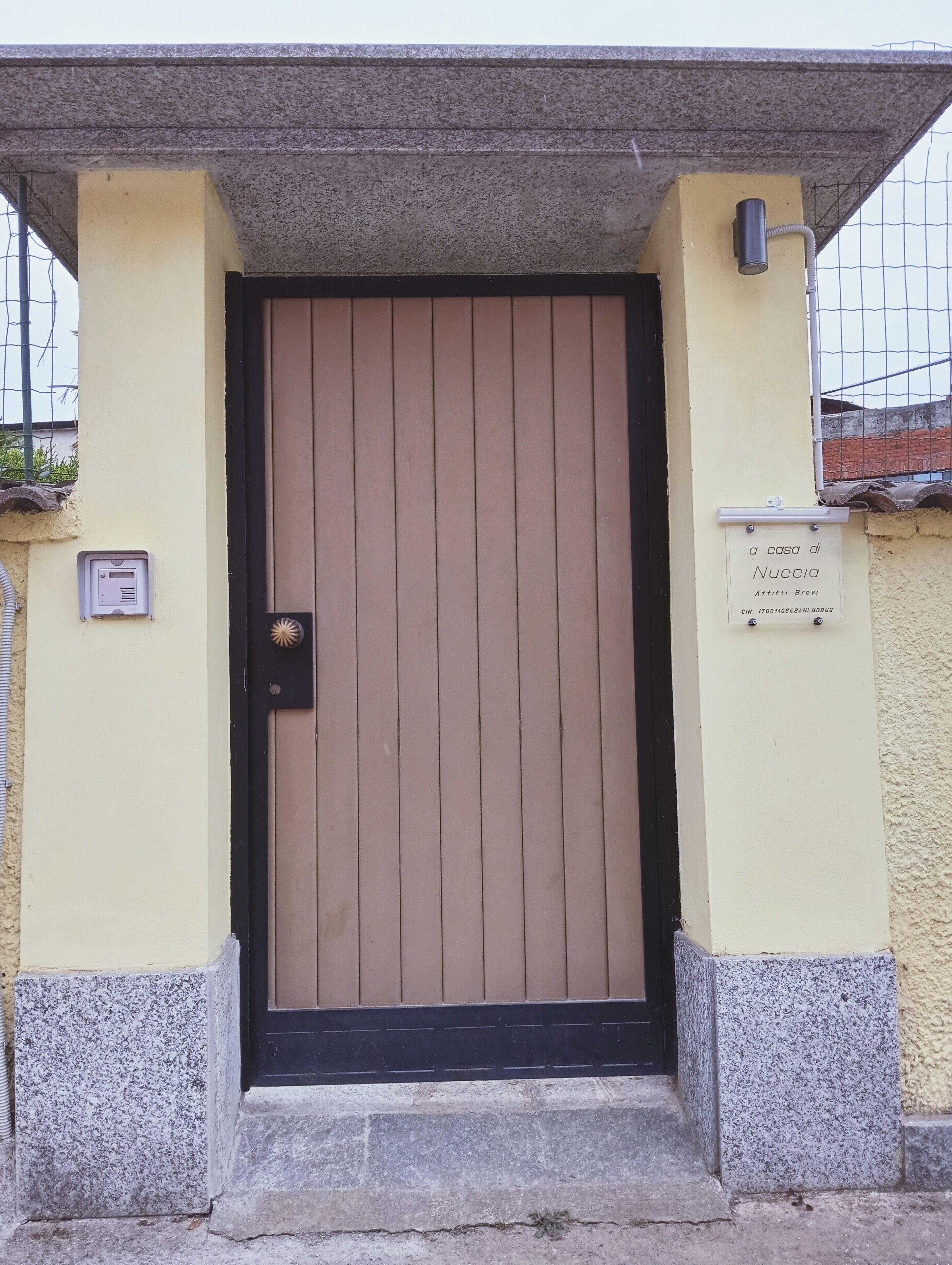A beige door with a black frame, a small electronic device on the wall to the left, and a sign above the door.