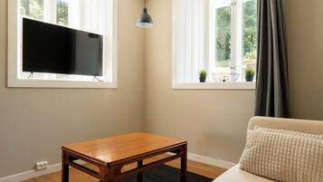 Una habitación con una mesa de madera, un sofá, un televisor y dos ventanas con cortinas.