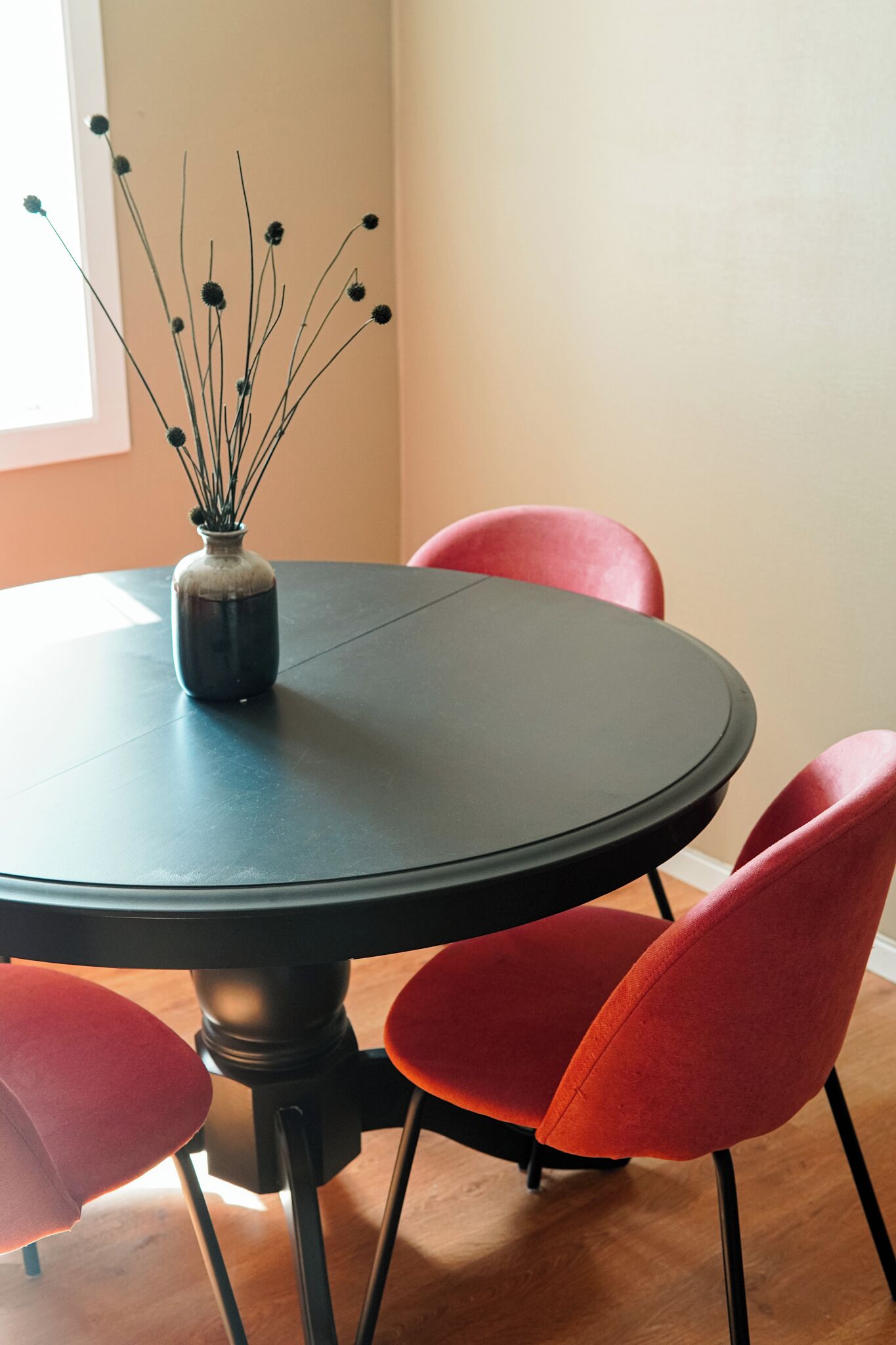 Una mesa redonda con un florero de flores secas, rodeada por cuatro sillas rojas.