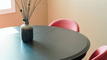 Una mesa redonda con un florero de flores secas, rodeada por cuatro sillas rojas.