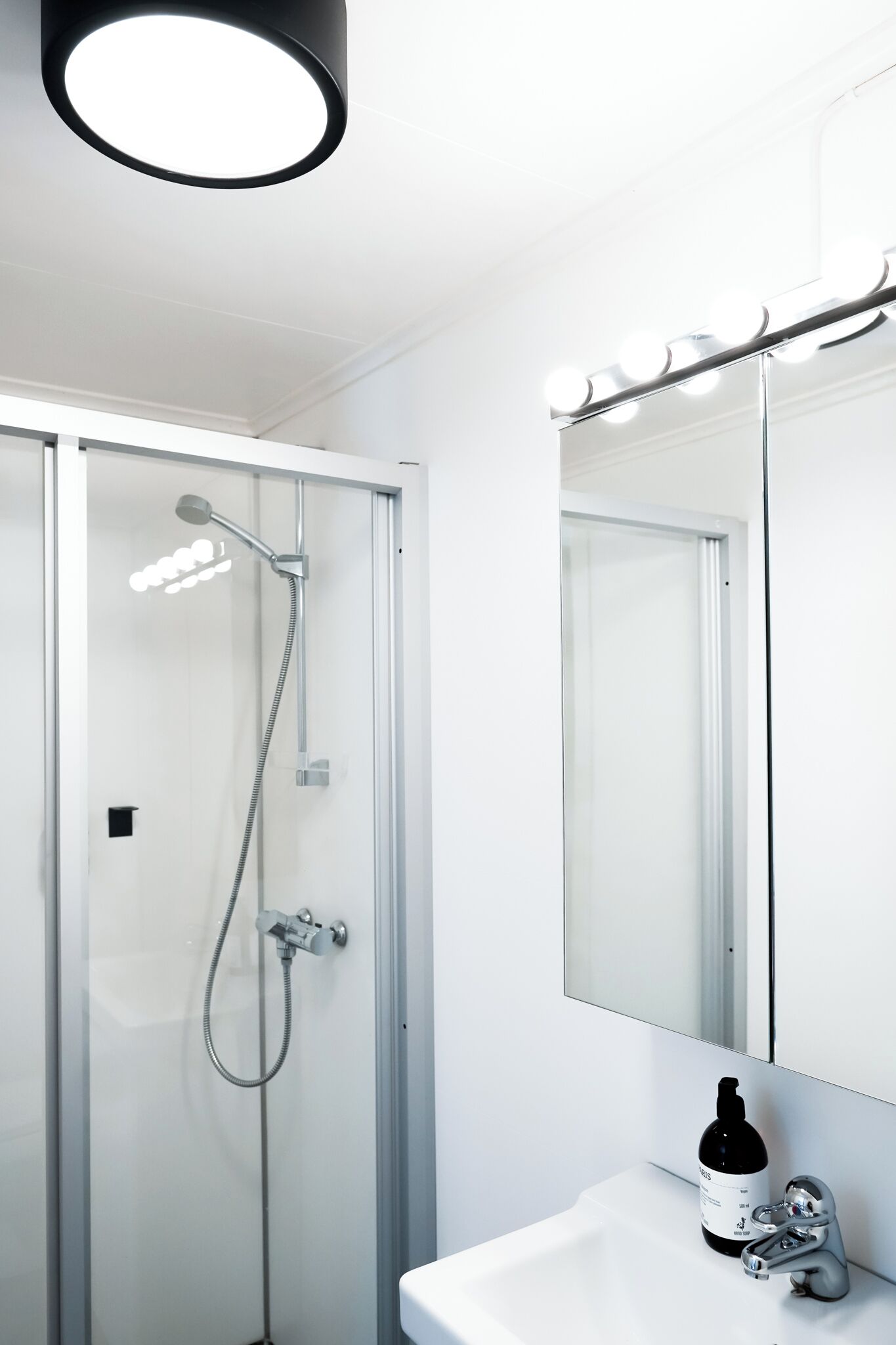 Ein modernes Badezimmer mit einer Duschkabine aus Glas, einem weißen Waschbecken und einem Spiegel mit Beleuchtung darüber.