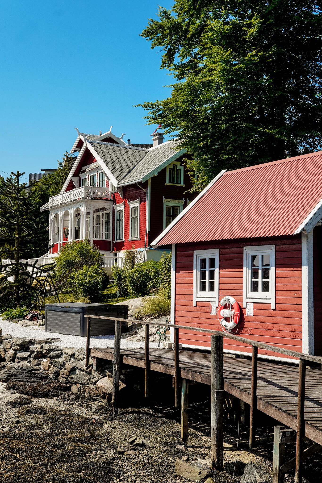 A red wooden house with a balcony and a lifebuoy attached to a wooden dock.