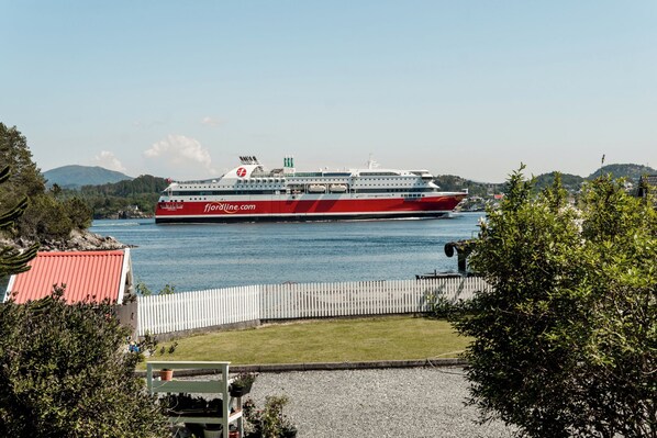 A large cruise ship docked at a port with a clear view of the surrounding landscape, including hills and a fenced area with greenery. - Villa Brattholmen (Oygarden)