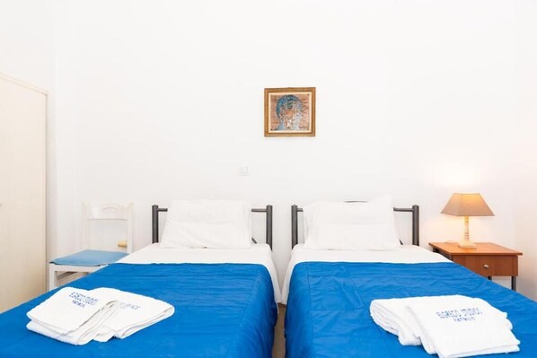 Une chambre d’hôtel avec deux lits, chacun recouvert d’une couverture bleue et agrémenté d’oreillers blancs. Un tableau encadré est accroché au mur, au-dessus des lits.