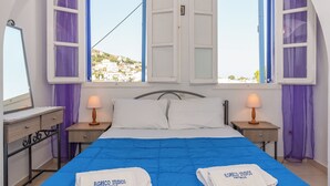 Ein Hotelzimmer mit einem Bett, zwei Nachttischen, zwei Lampen und Blick auf eine Hügellandschaft.