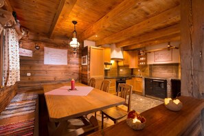 A cozy wooden cabin interior with a dining area, kitchen, and a fireplace.