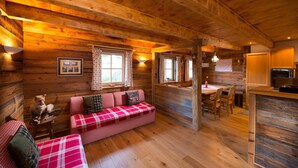 A cozy cabin interior with a wooden ceiling, a plaid sofa, a dining table, and a kitchen area. - Chalet in St. Martin with Sauna & Mountain Views (St. Martin am Tennengebirge)