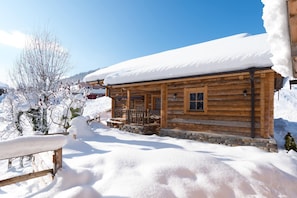 A wooden cabin with a snow-covered roof and a stone foundation.