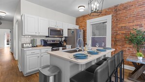 A modern kitchen with white cabinets, stainless steel appliances, and a brick accent wall. - Steps Away From Mass Ave in Heart of Indy with Balcony (Indianapolis)