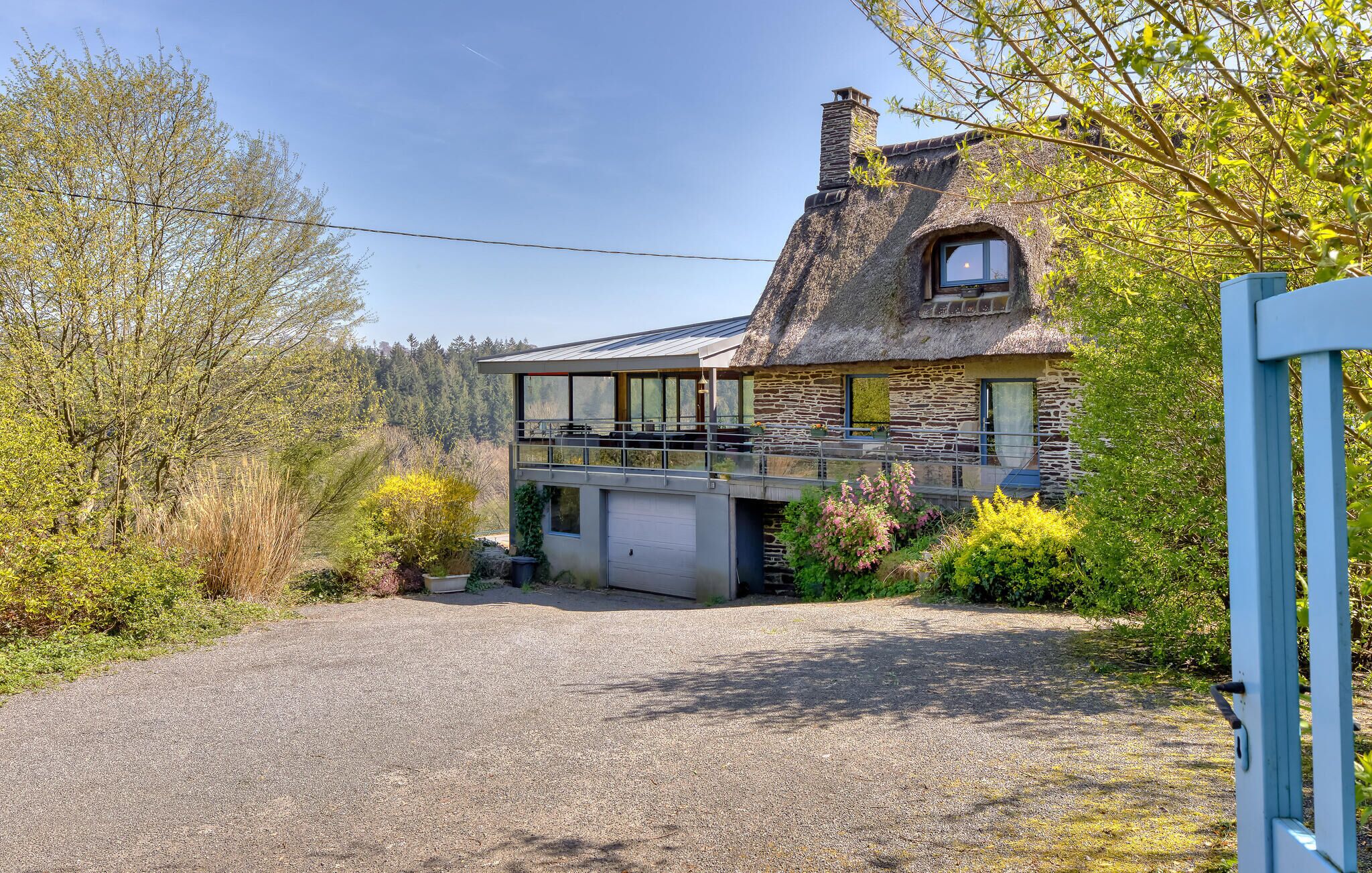 A two-story stone house with a thatched roof, a covered porch, and a gravel driveway.