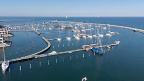 Een jachthaven met meerdere boten afgemeerd, een steiger en een vuurtoren in de verte.