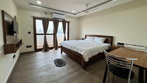 A hotel room with a bed, a desk, a chair, a TV, and a window with curtains. - HOTEL MADHAVA RESIDENCY (Kakinada)
