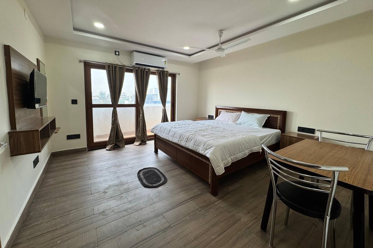 Une chambre d’hôtel avec un lit, un bureau, une chaise, une télévision et une fenêtre avec des rideaux.