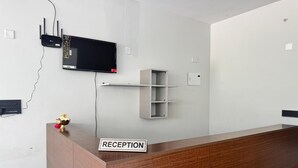 A reception desk with a sign, a flat-screen TV mounted on the wall, and a power outlet. - HOTEL MADHAVA RESIDENCY (Kakinada)