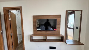 A room with a mounted TV on a wooden wall, a mirror, and a door with a wooden frame. - HOTEL MADHAVA RESIDENCY (Kakinada)