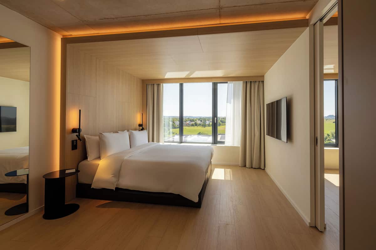 Una habitación de hotel moderna con una cama grande, un televisor de pantalla plana y un balcón con vistas a la ciudad.